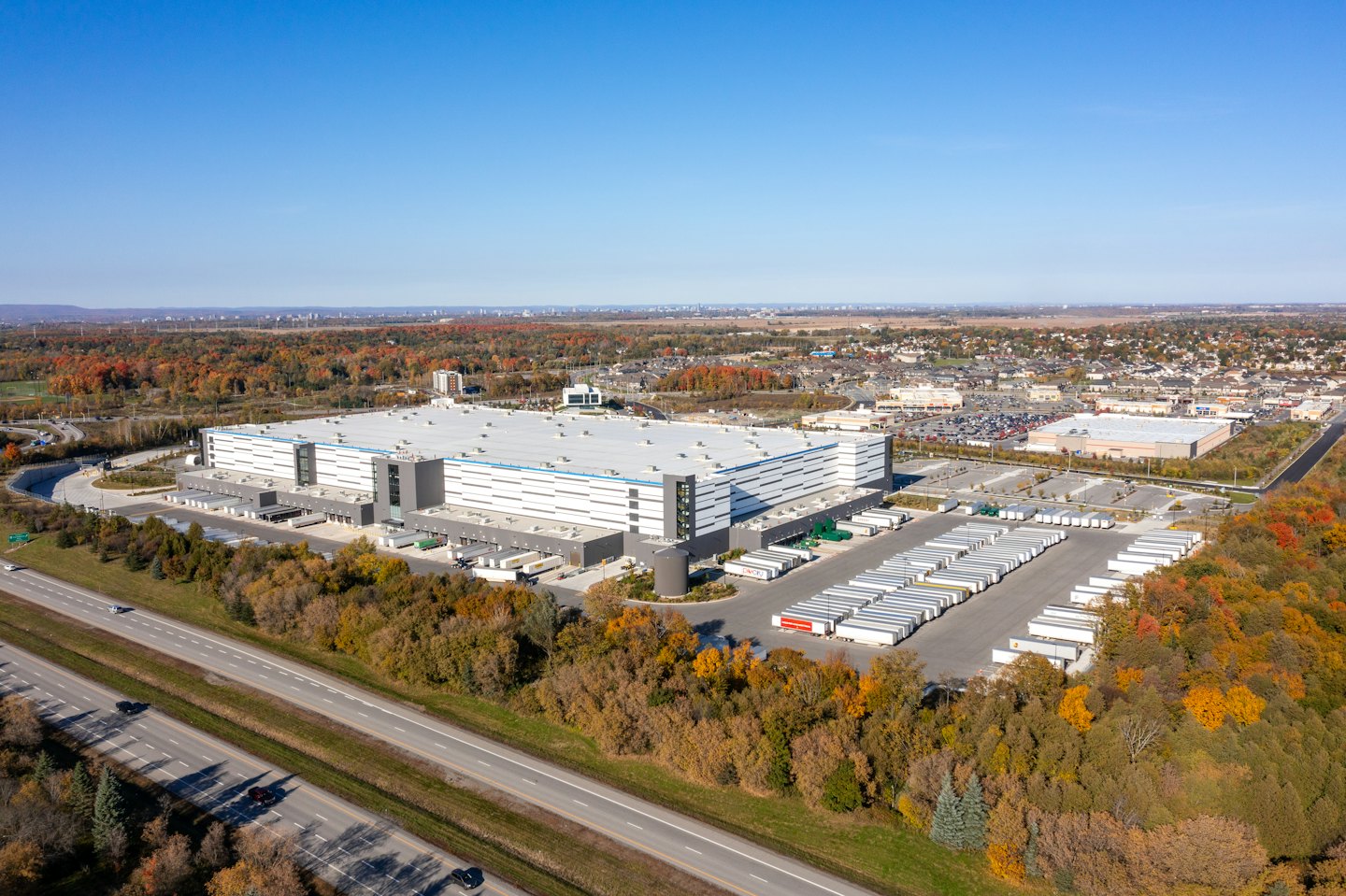 Large industrial warehouse with loading docks and semi-trucks near highway.
