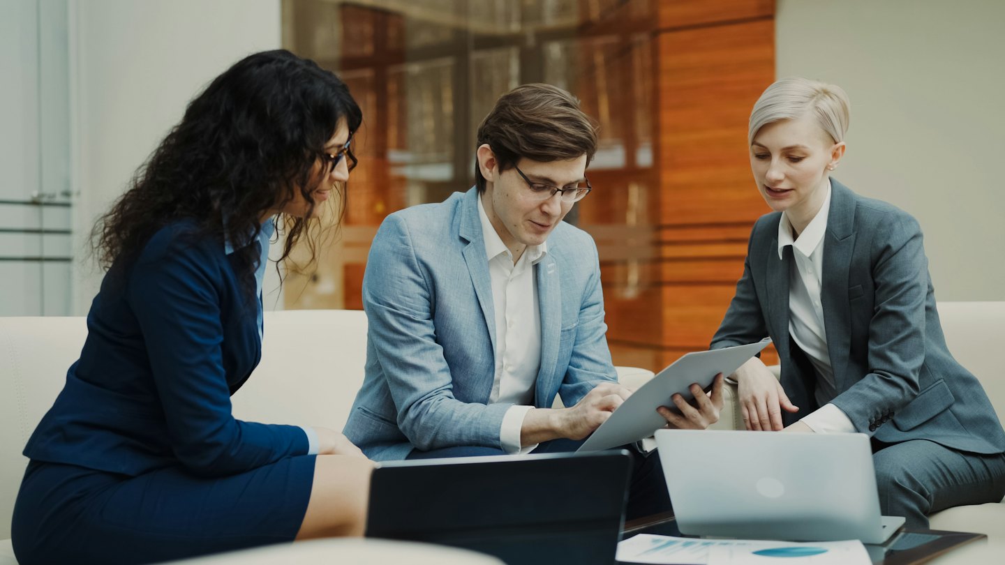 Three business people collaborate over a tablet and laptop.